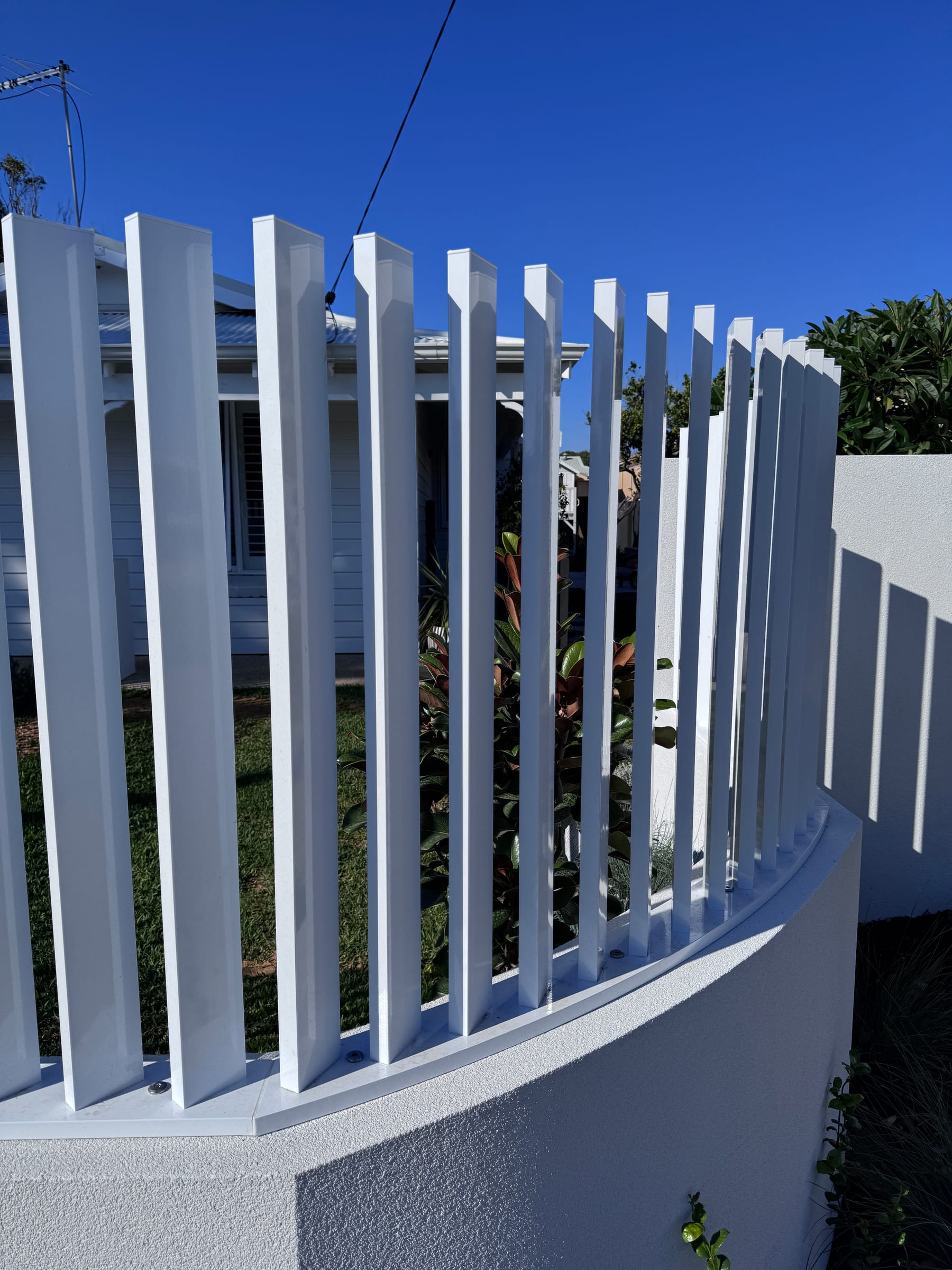 White aluminium verticals following a curved rendered wall