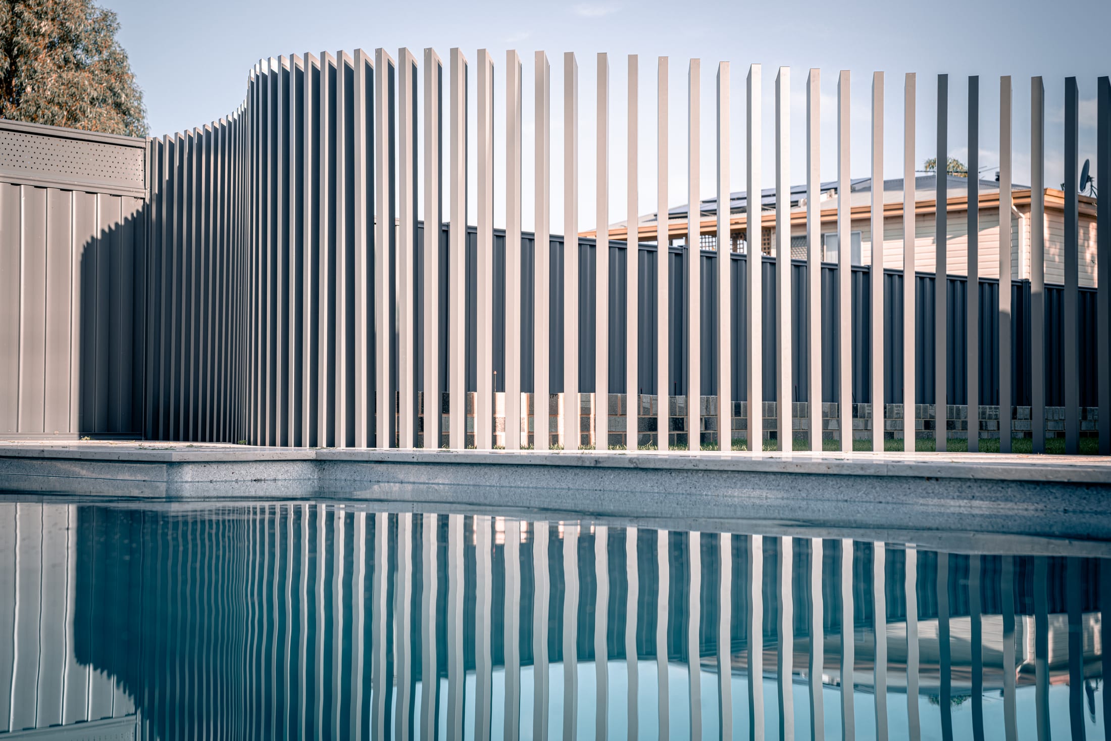 A stone grey aluminium pool fence sweeping into a curve, reflected in still pool water