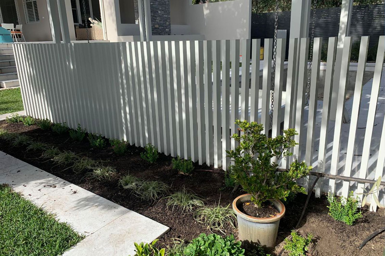 A white aluminium fence along a freshly planted garden bed, screening a pool beyond