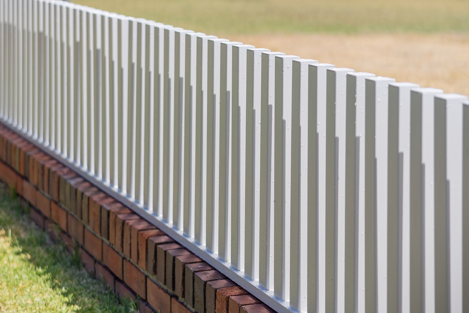 A white aluminium fence on a red brick plinth, running away along a lawn