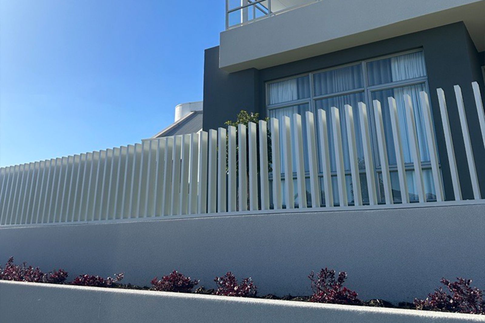 A soft white aluminium fence stepping up a rendered wall in front of a dark grey house
