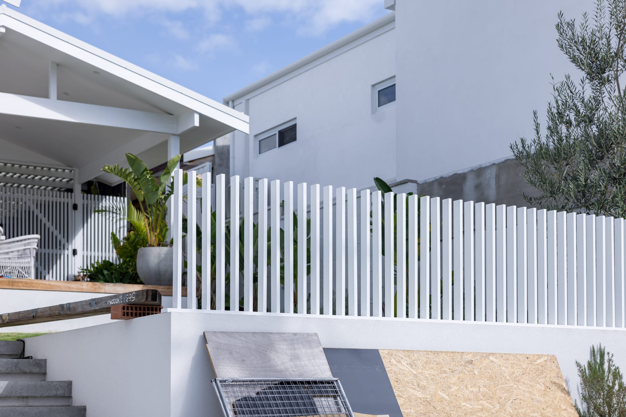 A white aluminium fence and matching vertical gate beside an alfresco area