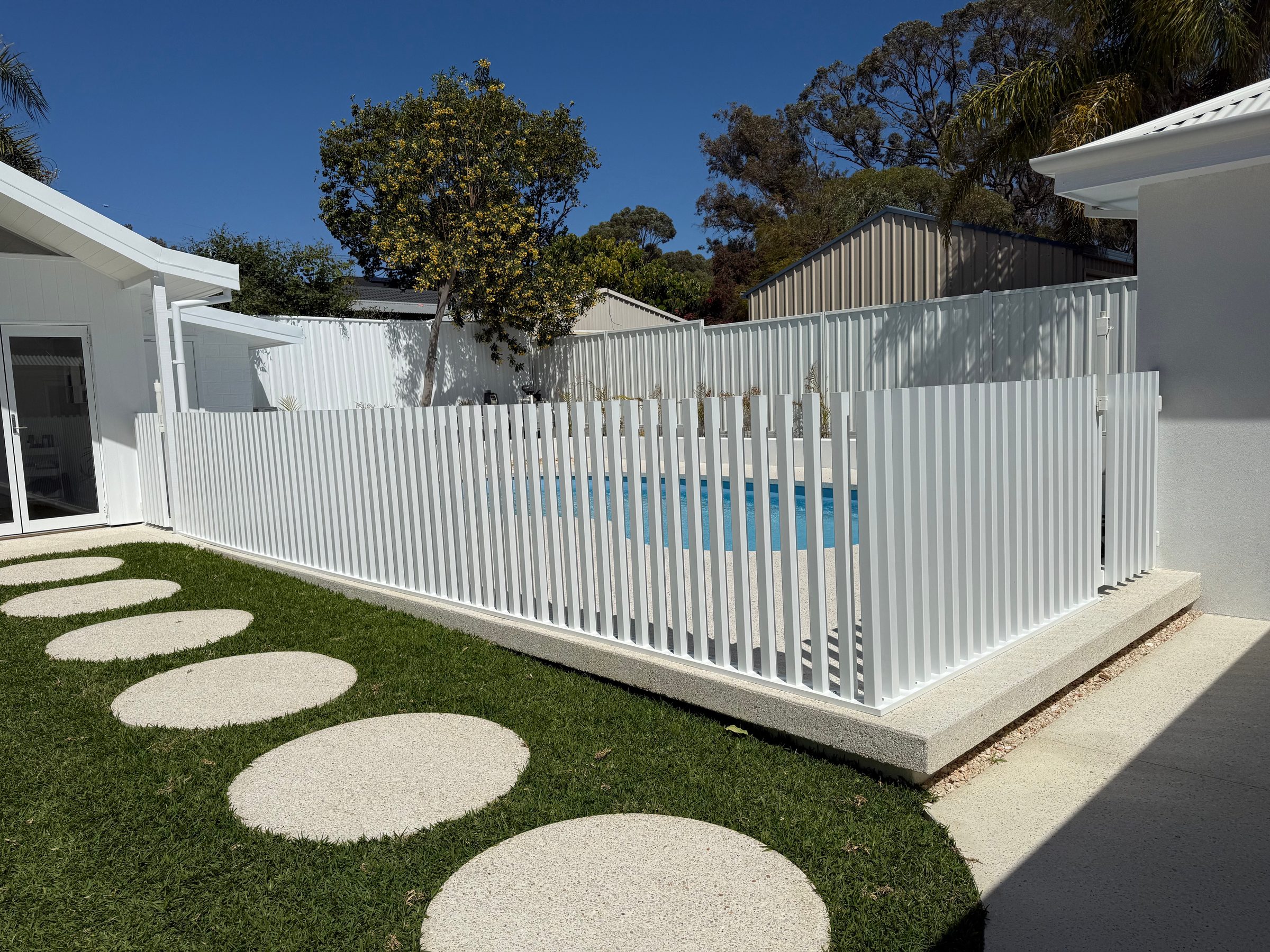 A white aluminium pool fence returning around a corner in bright sun