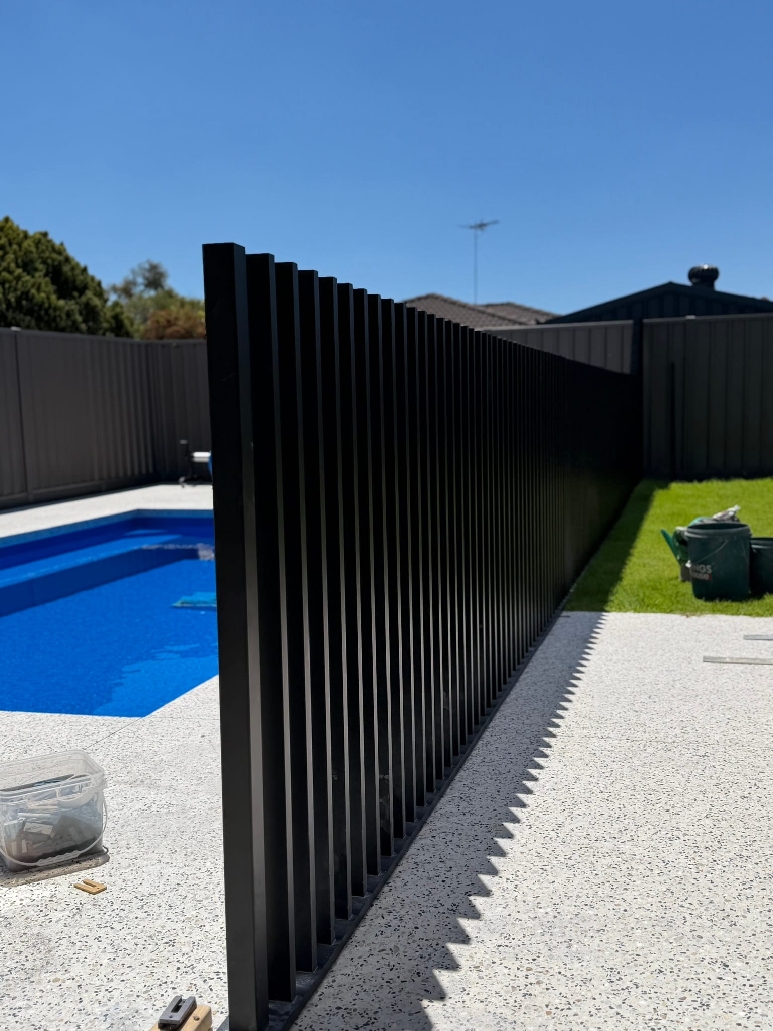 A freshly installed fence run on exposed aggregate paving, with the installer's tools still on site
