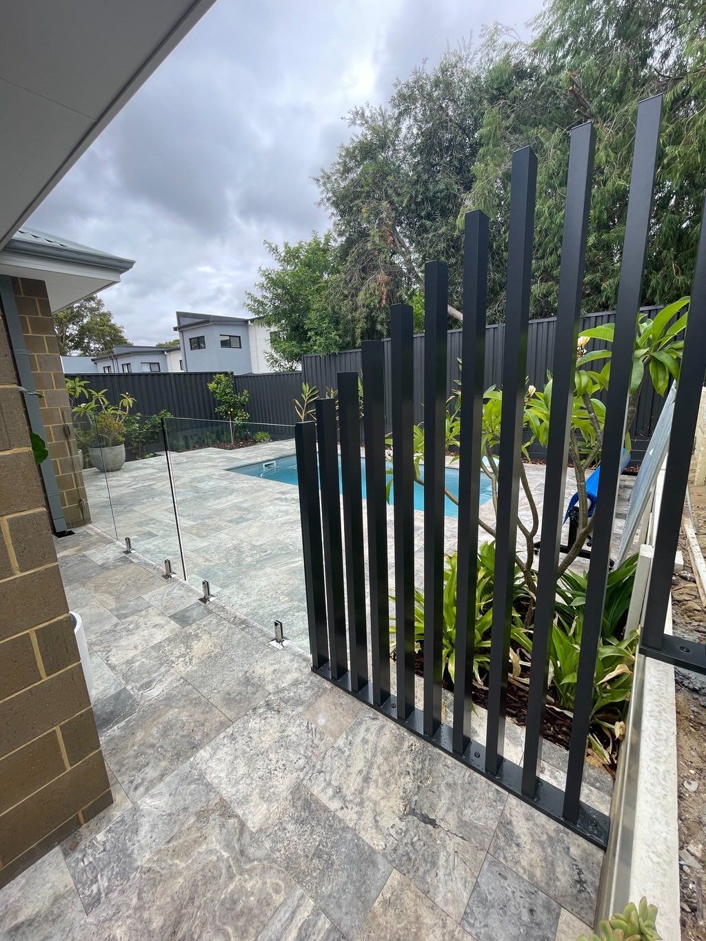 A black aluminium fence running beside a frameless glass pool barrier
