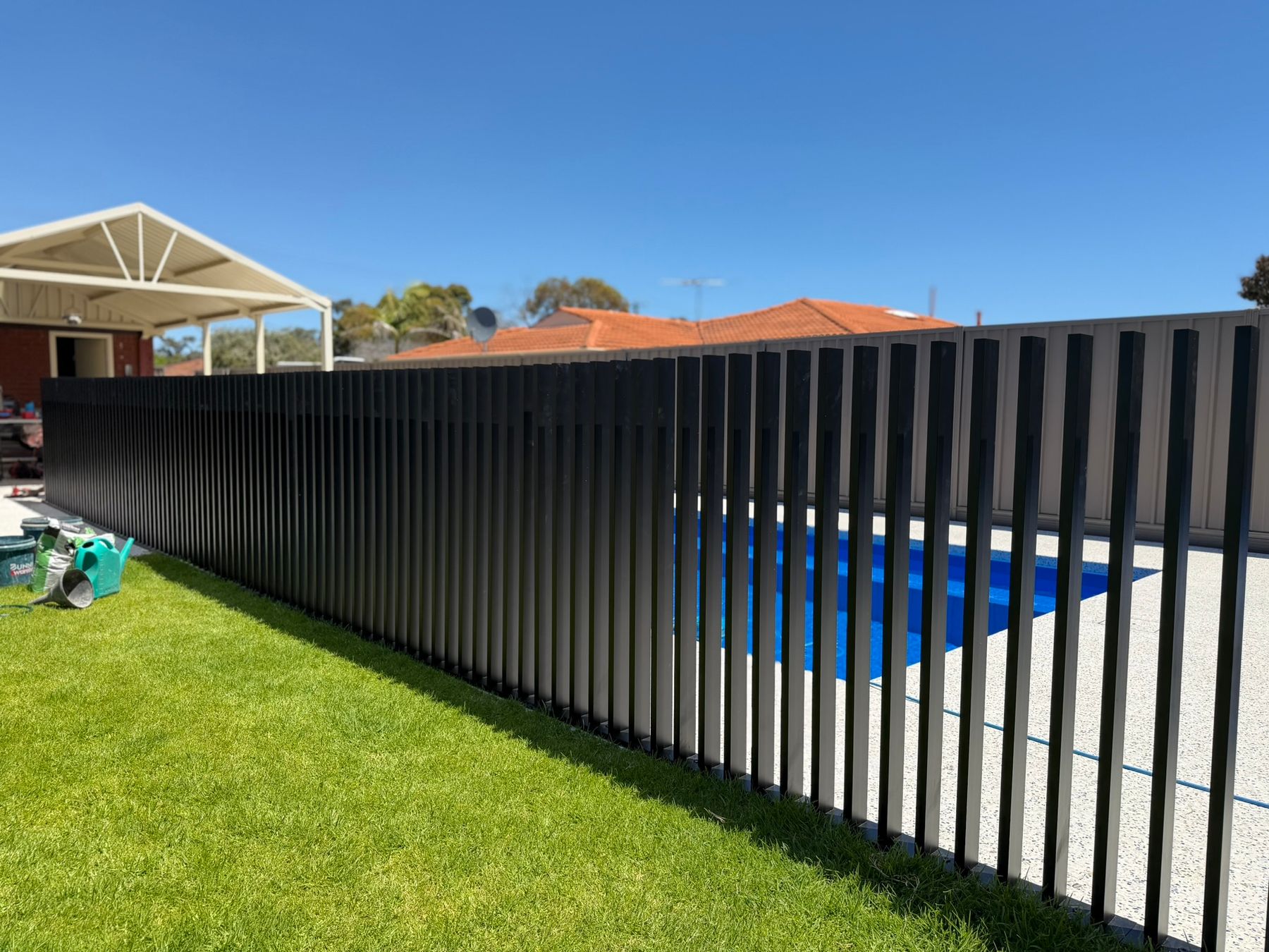 A matte black aluminium pool barrier along a paved surround