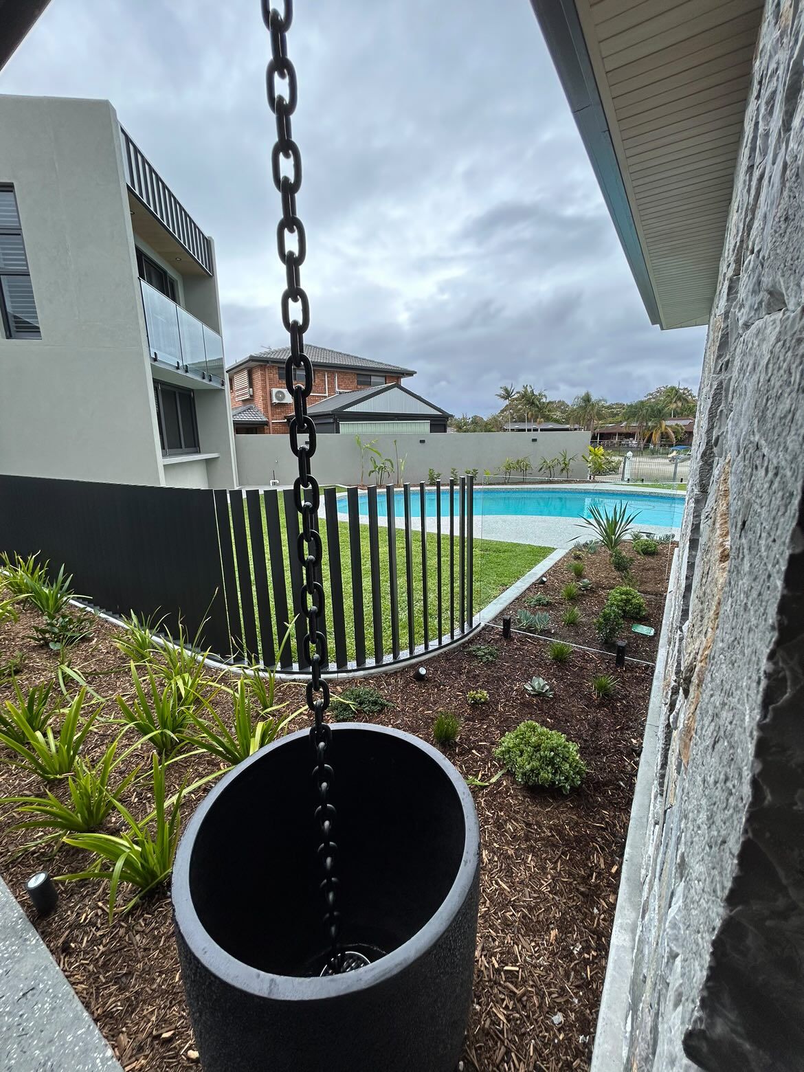 A monument grey aluminium fence curving around a garden bed