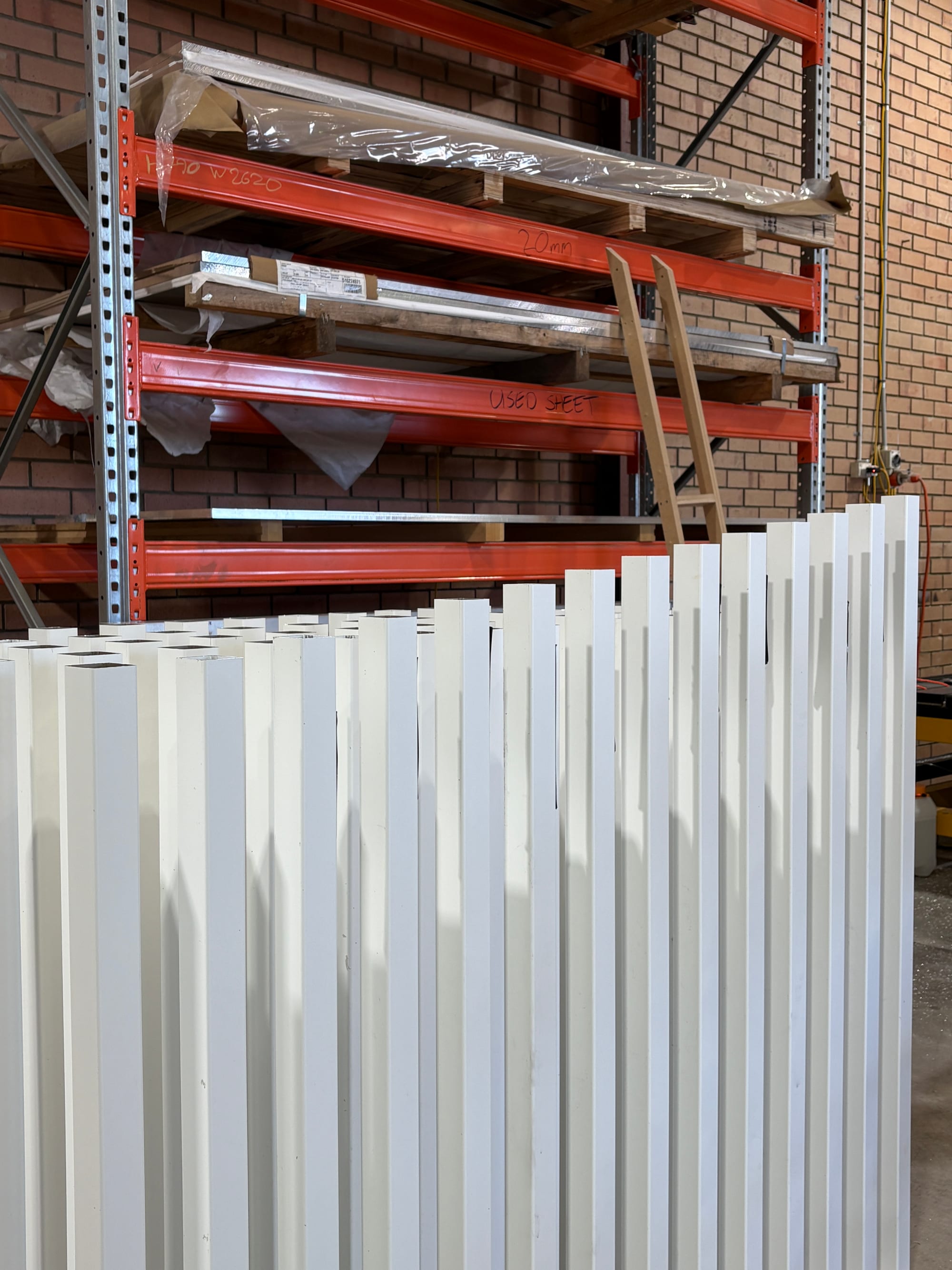Finished aluminium sections stacked on pallet racking in the AFS workshop
